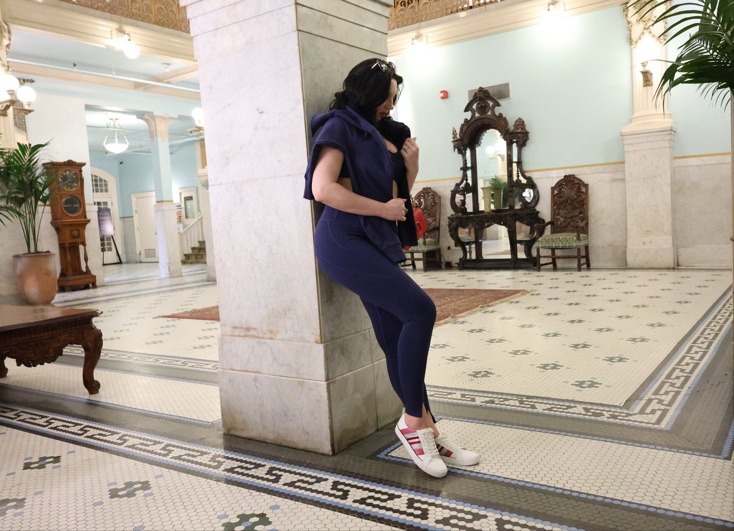 Person in a purple outfit standing in an elegant interior setting with marble columns and decorative furniture.