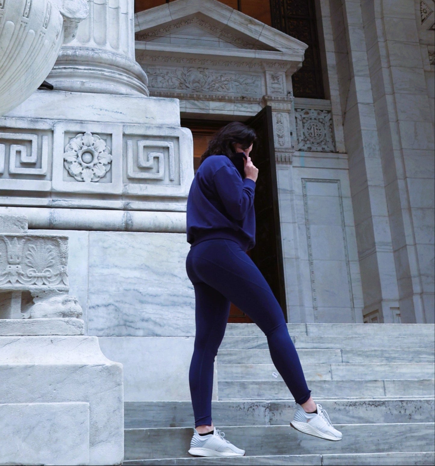 Person in a blue outfit standing on stone steps of a classical building