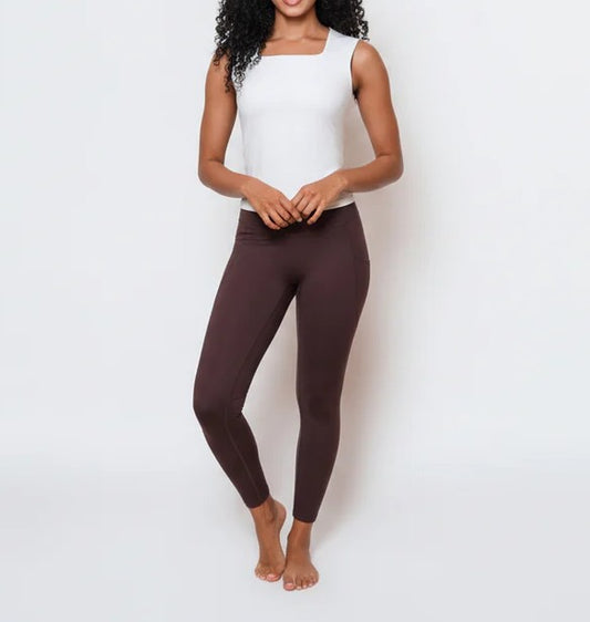 Woman wearing brown leggings and a white top on a light background