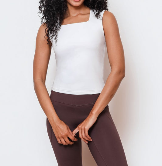 Woman wearing a white tank top and espresso brown leggings on a plain background