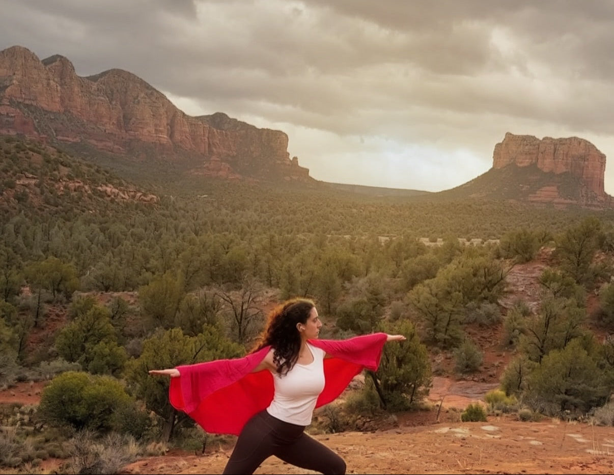 Woman with a pink wrap standing in a desert landscape with mountains under a cloudy sky