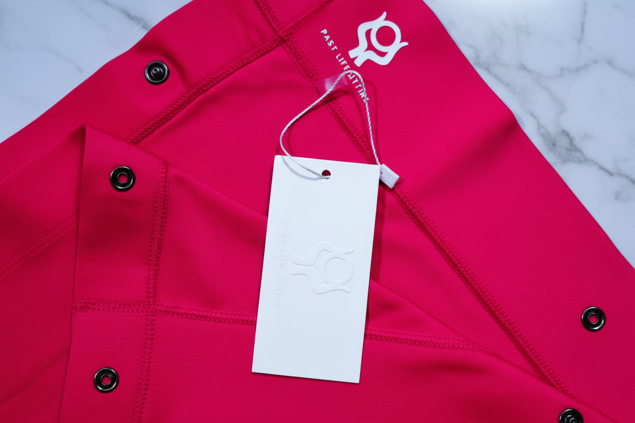 Pink shawl with a white tag and brand logo on a light gray background