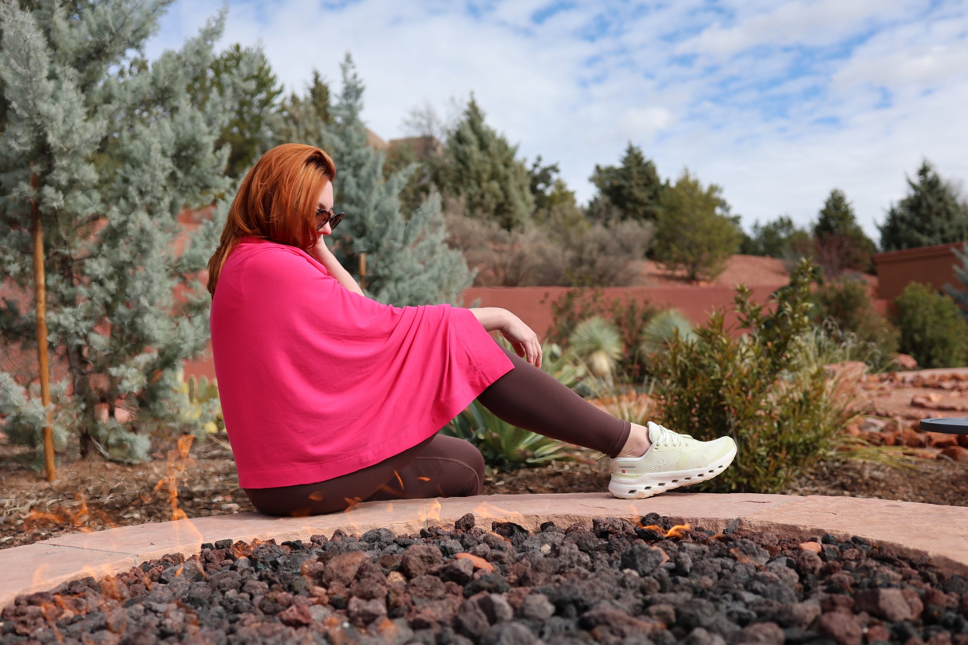 Person in a pink dress sitting on a stone path with trees and a building in the background